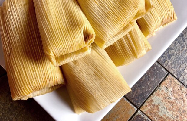 Una pila de tamales envueltos en hojas de maíz sobre un plato blanco.