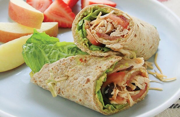 Rodajas de manzanas y fresas junto a una envoltura de pollo desmenuzado en un plato azul.