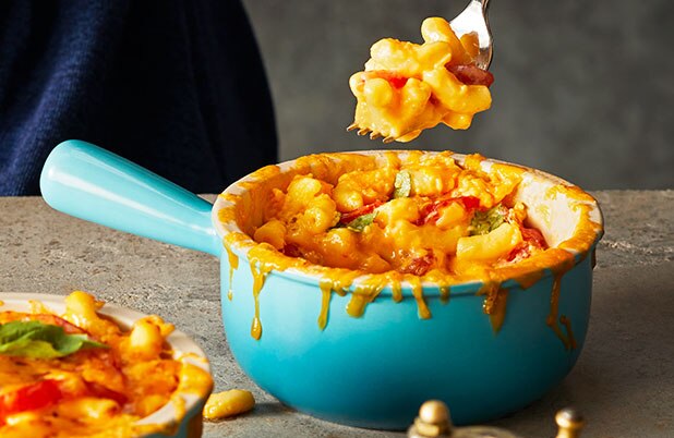 Macarrones con queso con tomate y albahaca en un bowl de cerámica azul sobre un mostrador de granito.