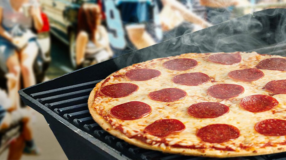 Una pizza de pepperoni echa vapor y se cocina en una parrilla de gas enfrente de gente sentada.