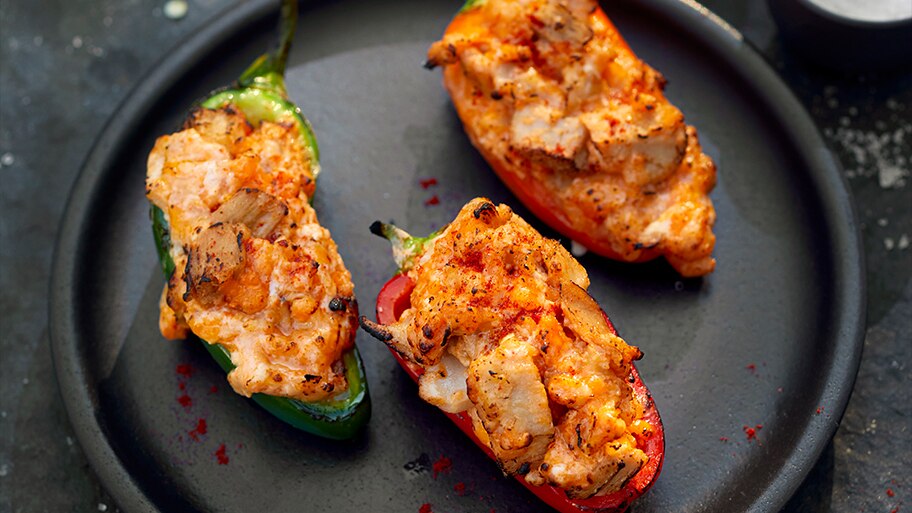 Un plato negro con pimientos rojos y verdes rellenos de Mindful Chik'n con salsa y queso.