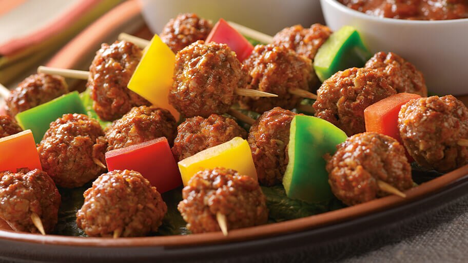 Plato lleno de brochetas de albondiguitas y pimientos de colores.