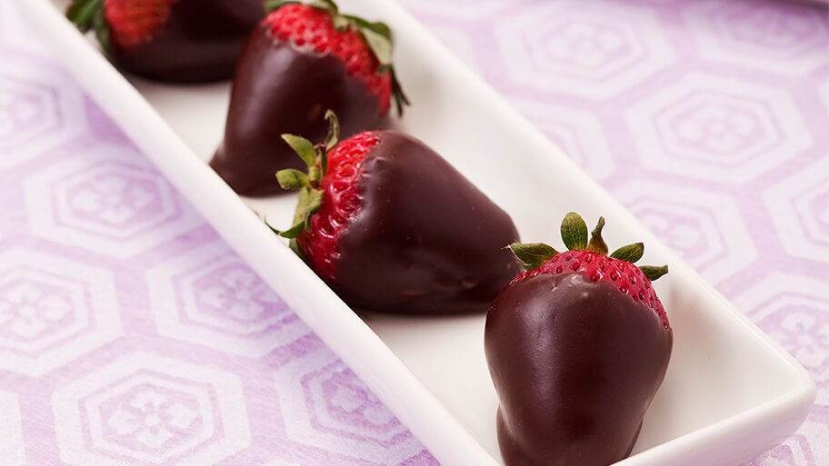 Fresas cubiertas de chocolate en una bandeja de cerámica sobre un moderno mantel lila.
