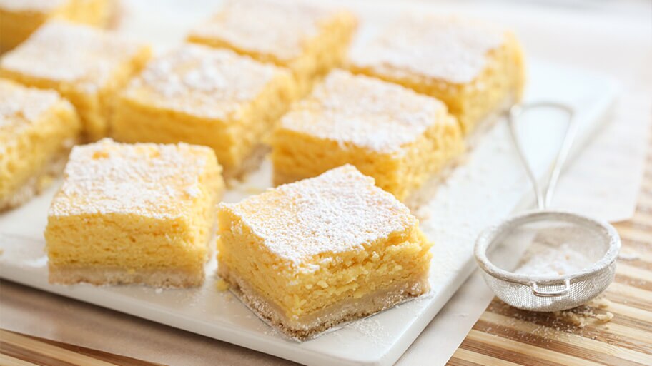 Barra cremosa de limón con azúcar glaseado por encima sobre una tabla de mármol con un cernedor de harina.