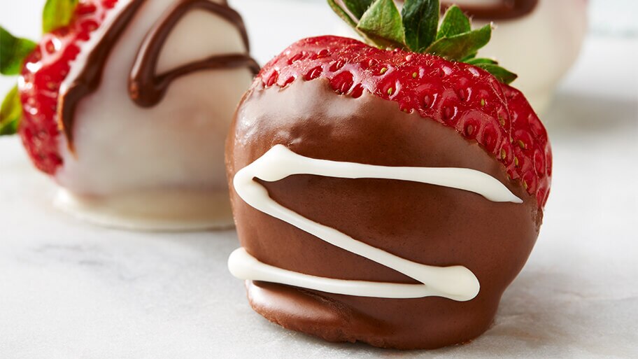 Primer plano de una fresa cubierta con chocolate con leche y una fresa cubierta de chocolate blanco sobre una mesa de mármol.
