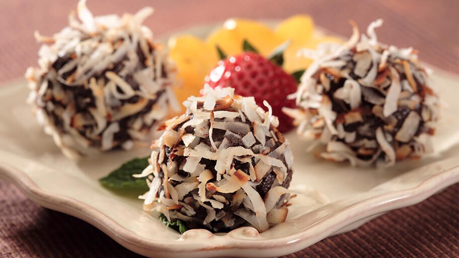 Trufas de chocolate cubiertas con coco tostado sobre una bandeja de cerámica con fruta fresca.