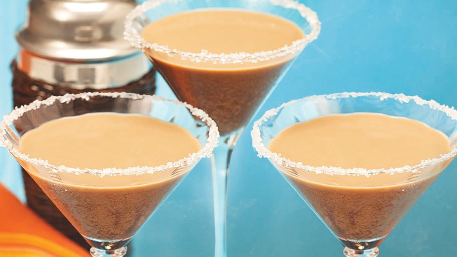 A martini shaker behind 3 martini glasses with sugar rim filled with Coffee Abuelatini.
