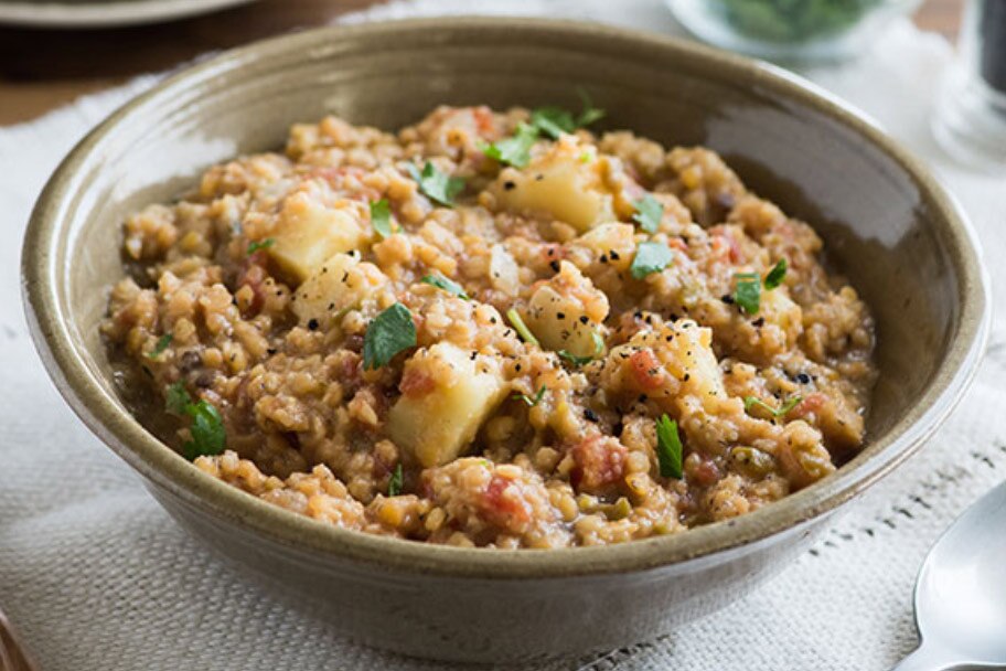 A black plate of red and green bell peppers stuffed with saucy and cheesy Mindful Chik'n.