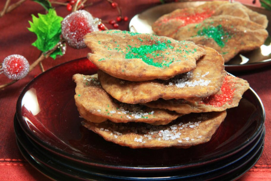 Una pila de buñuelos de chocolate en platos de color marrón y un mantel rojo cerca de ramitas de acebo.