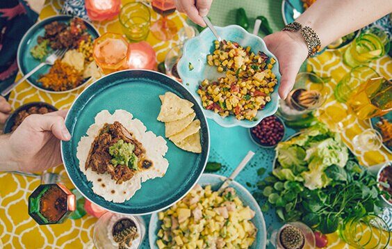 Overhead photograph of hands passing plates and eating food at a feast.