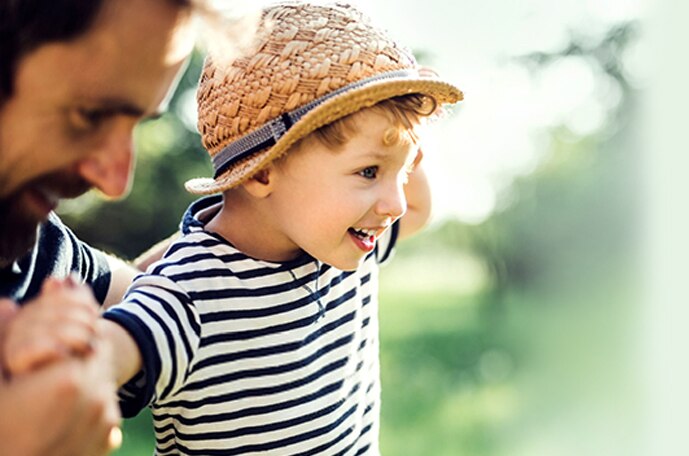 A young child in a black and white shirt and straw hat stands with their arms outstretched.