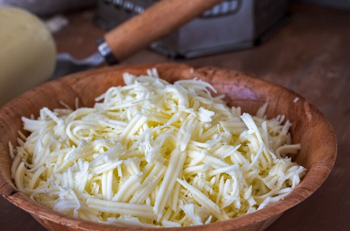 A pile of shredded cheese in a wood bowl.
