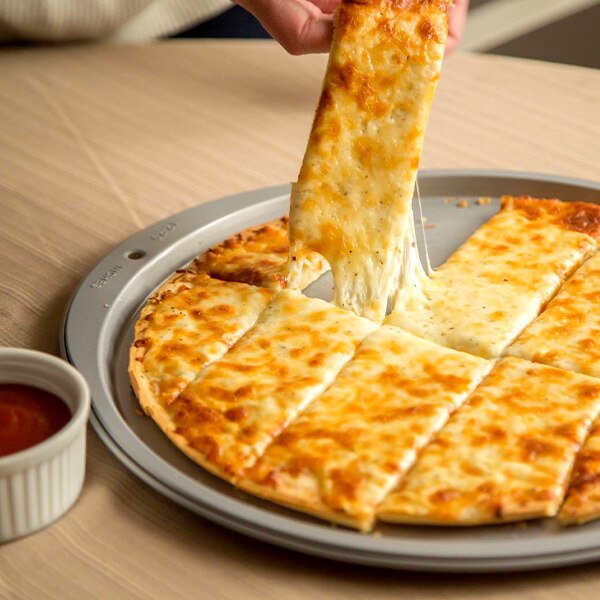 A hand lifts a Cheesy Pizza Dipper from the backing sheet beside a cup of marinara.