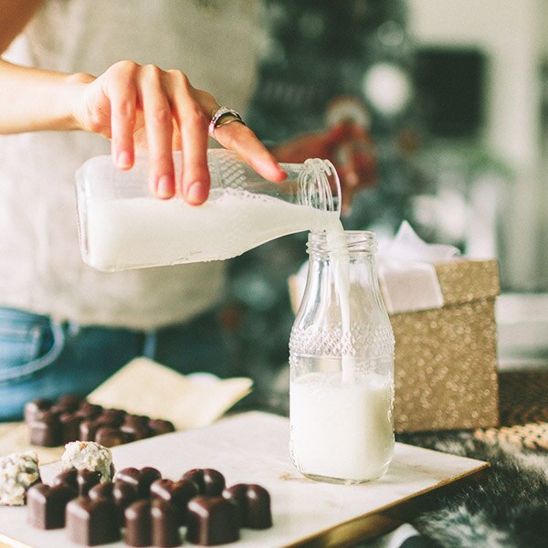 Una mujer vierte leche de una jarra de vidrio a otra.