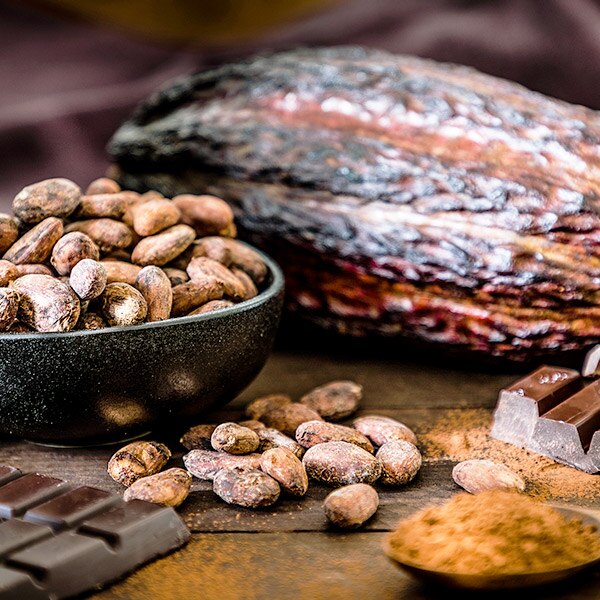 Pieces of chocolate scattered around cocoa beans and leaves on a wooden table.