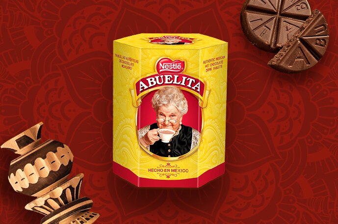  Packaging of ABUELITA tablets beside tablets and a molinillo on a red background with mandalas. 