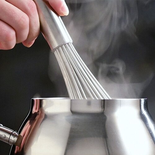 A whisk stirs steaming hot chocolate in a silver pot.