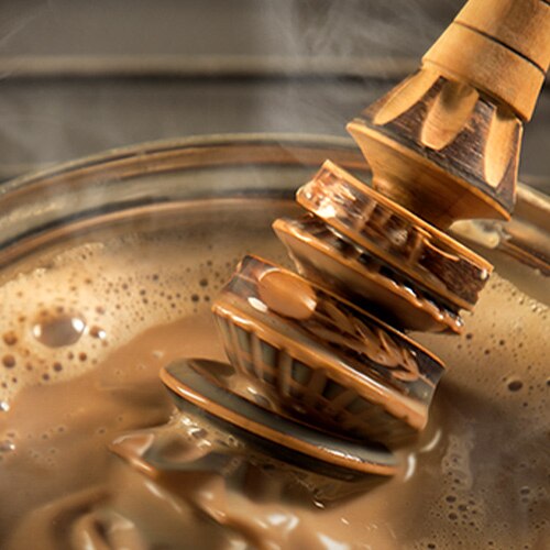 A molinillo stirs steaming hot chocolate.