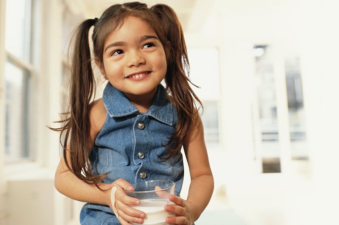 A young girl with pigtails smirks while drinking a glass of NIDO.