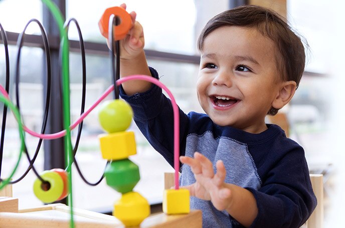 A young boy smiles and plays with his maze toy.