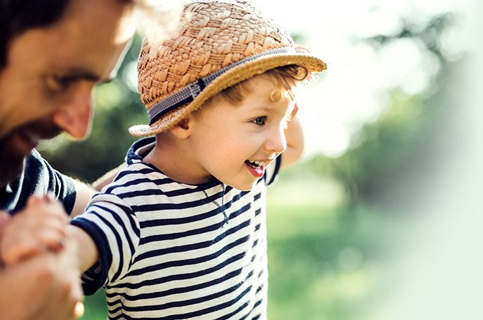 A young boy wearing a hat runs with his dad.