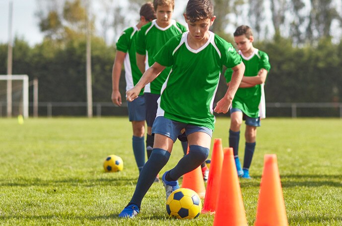 A soccer team in green jerseys dribble a ball through orange cones.