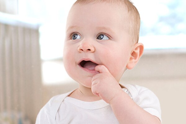 A baby holds his finger up to his mouth.