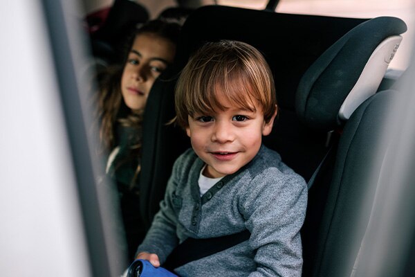 A young boy smiles as he sits in the back seat of the car buckled into a car seat.
