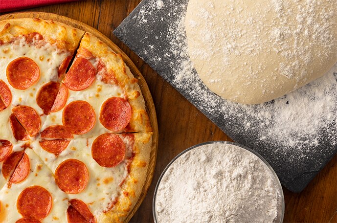 Una bola de masa rodeada de harina sobre una superficie de madera.