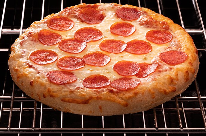 Una mano saca del horno una pizza supreme sobre una pala de metal para pizza.