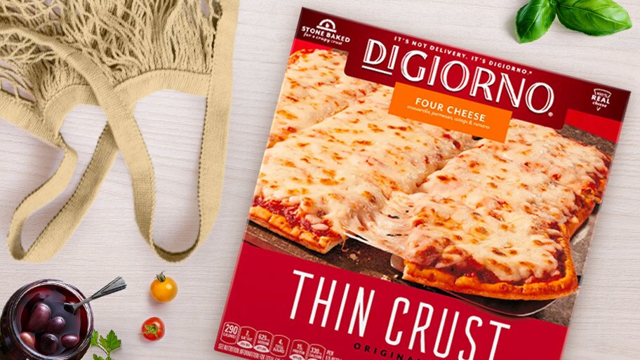 A hand holds a package of DiGiorno Four Cheese Thin Crust pizza in front of a freezer.