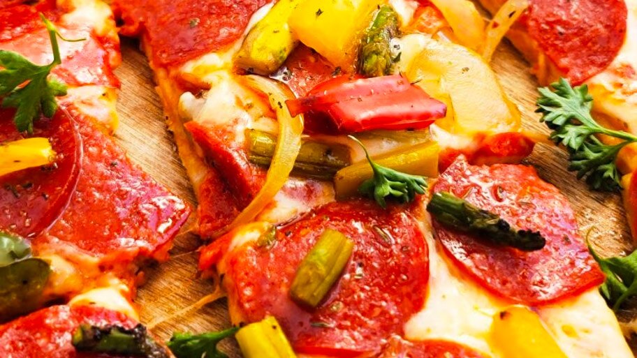 A DiGiorno pepperoni thin crust pizza topped with peppers, onions and asparagus cut in squares on a wooden paddle.