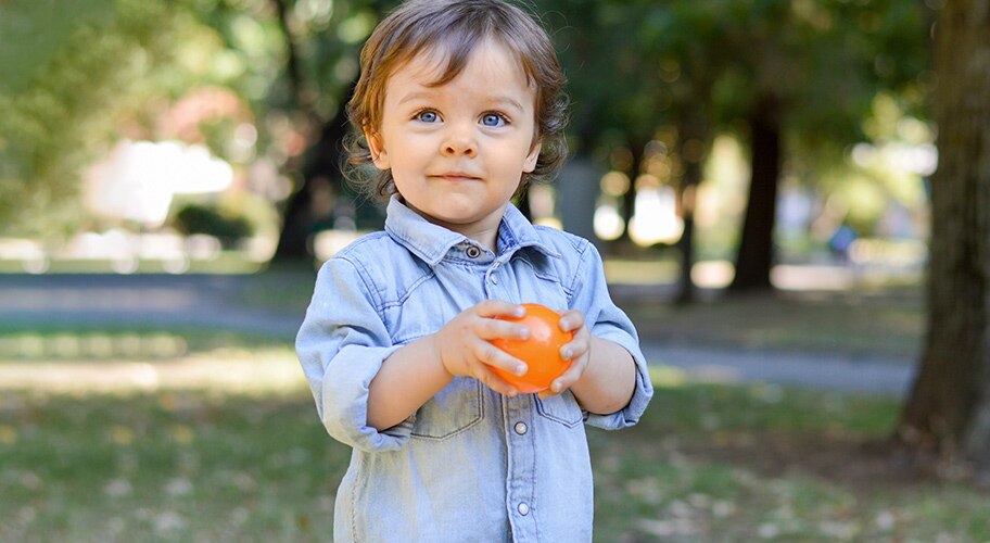 toddler with a orange ball outside.