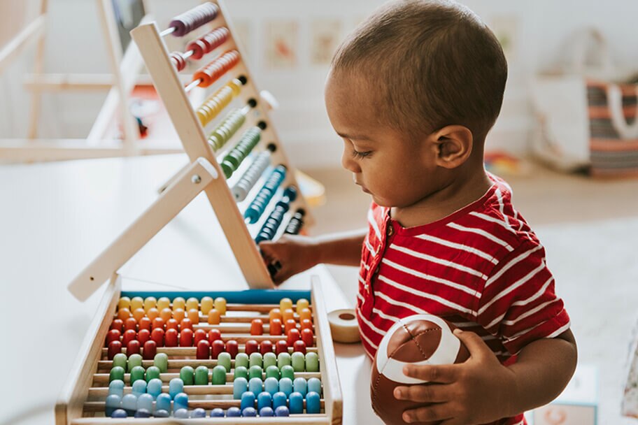 Child playing with a toy while holding a ball in a playroom.