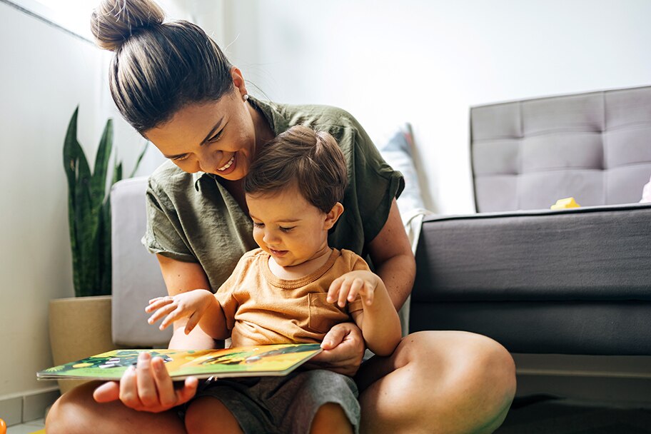 Woman reading a story book to her toddler in a bedroom.