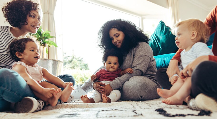 Group of moms with toddlers in their laps in a living room.
