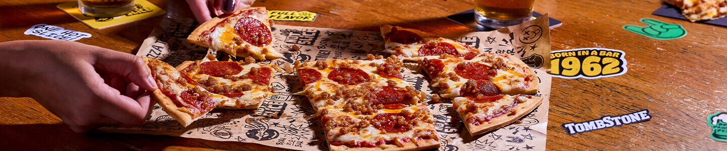 Pepperoni and cheese pizza on platters with people holding slices in the background.