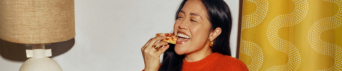 Woman reclining on an orange couch smiling to camera about to take a bite of Lean Cuisine spaghetti with meatballs.