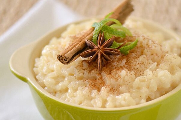 A green dish of rice pudding with a cinnamon stick, star anise, and a sour lemon spiral garnish.