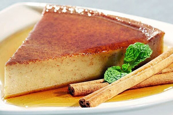 A slice of flan with cinnamon sticks and fresh mint.
