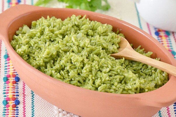 A clay dish filled with green rice on a colorful table cloth.