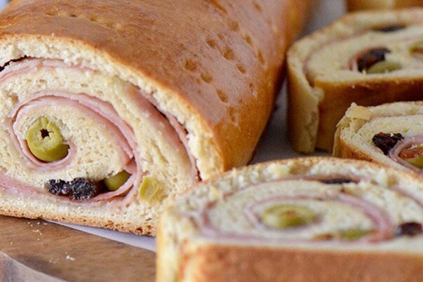 A loaf of sliced Venezuelan ham bread on a cutting board.