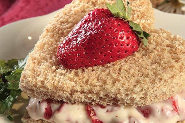 A strawberry and cream cheese sandwich cut into a heart shape on a plate.