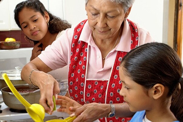 A young woman watches her grandmother help her little sister with a manual juicer.