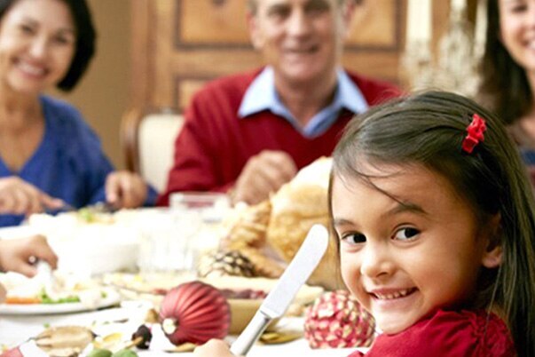 A family smiles for a photo as they gather around a festive table for Christmas dinner.