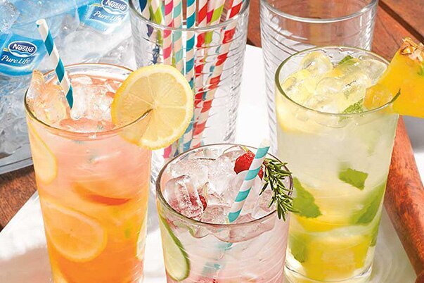 Bottled water, glasses of iced tea, fruit water, and lemonade surround a glass filled with paper straws.