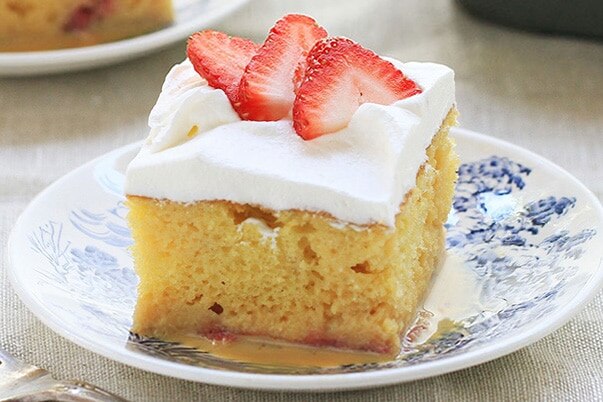 Strawberry tres leches cake on a white and blue plate.
