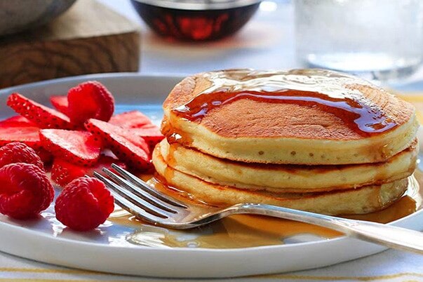 A plate of pancakes with a fork and strawberry slices.