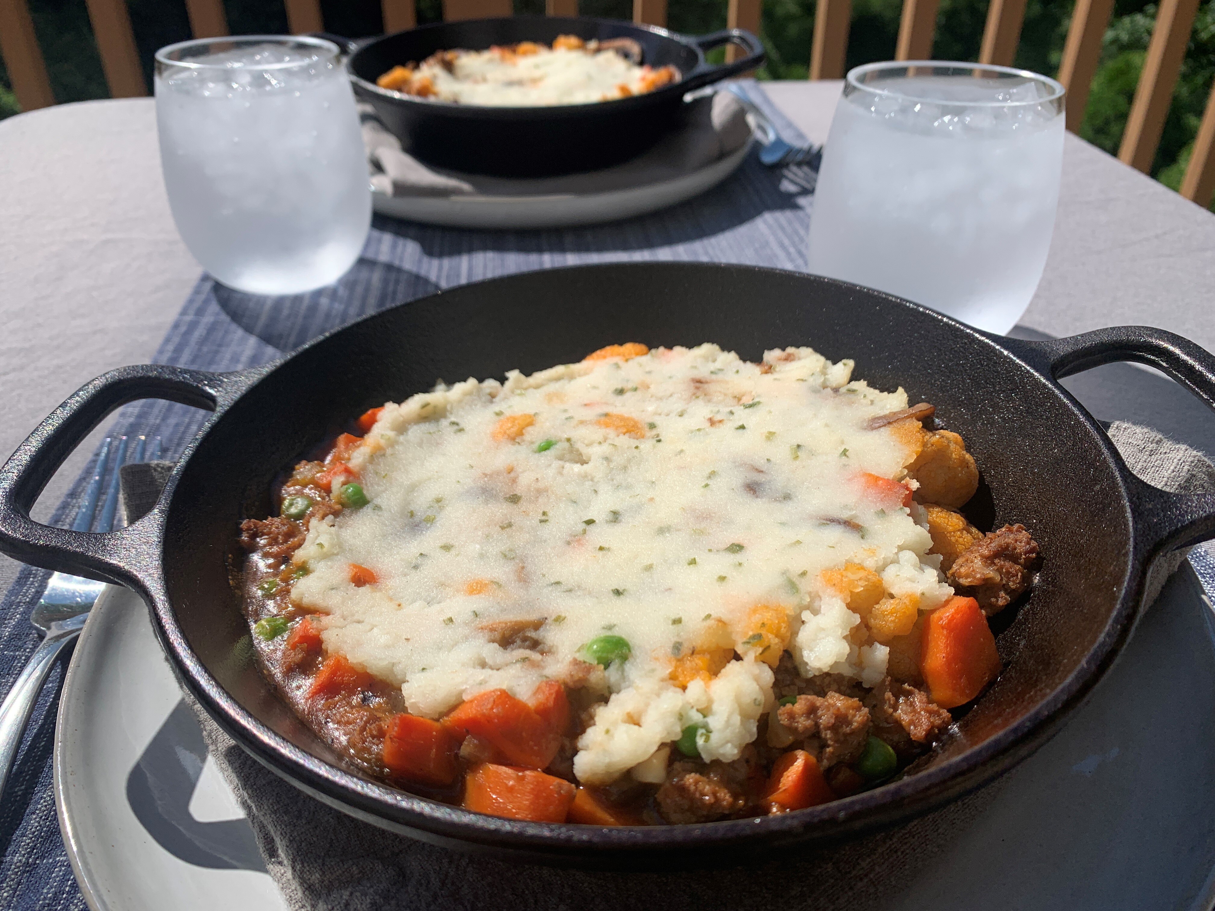 Table set for two with a cast iron skillet containing shepherd's pie and two chilled glasses of water.