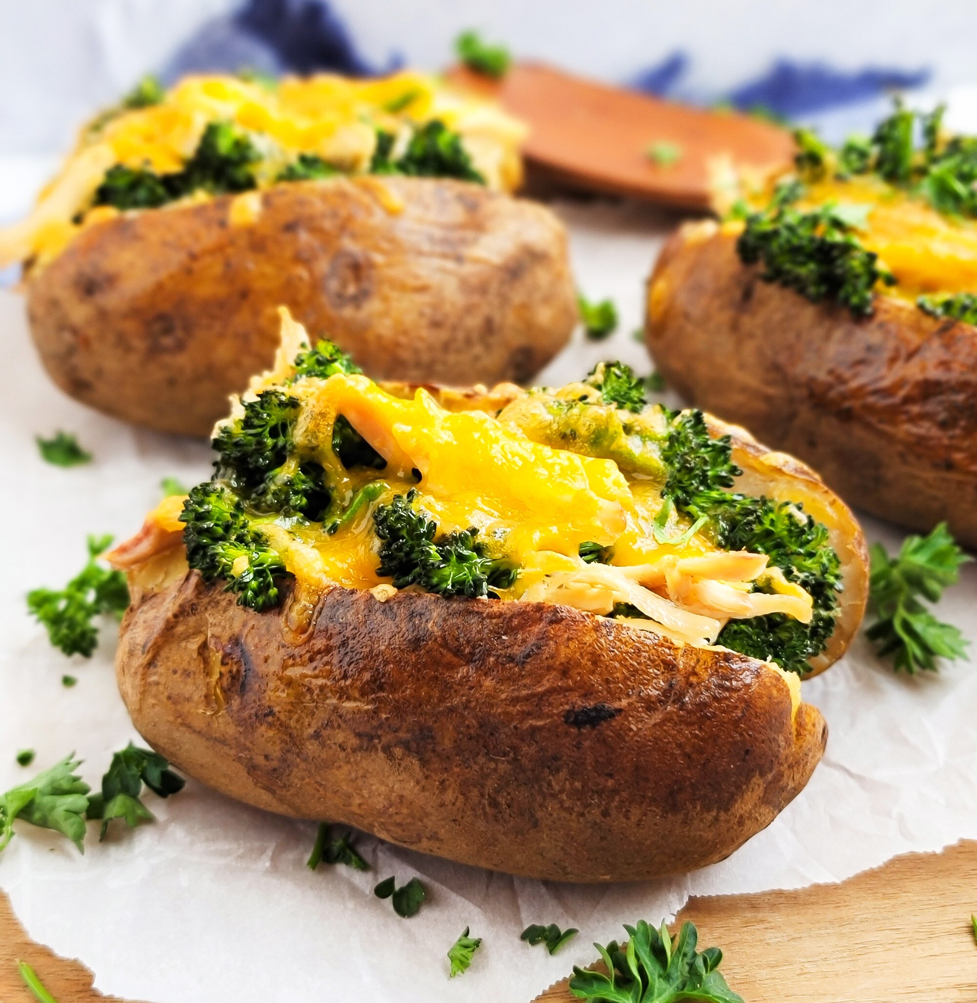 Three baked potatoes loaded with cheese, chicken and broccoli on a cutting board with parchment.